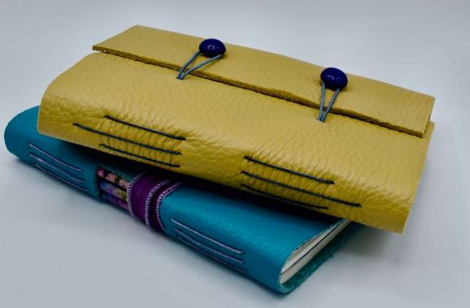two leather bound journals - one yellow, one blue, on top of each other