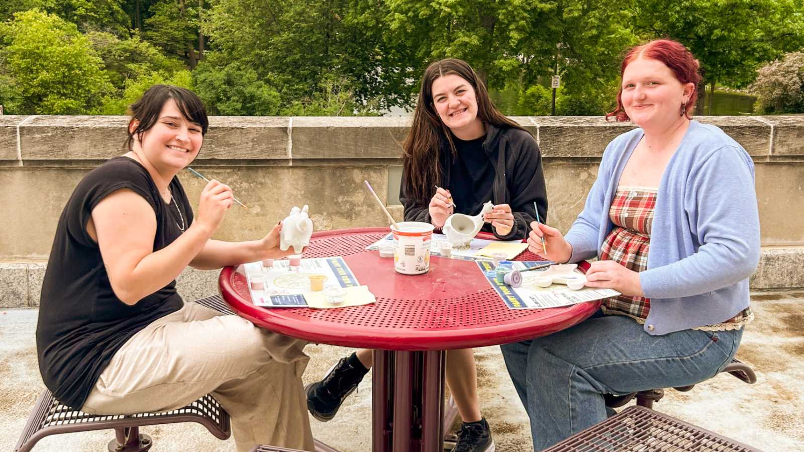 students around table painting pottery and smiling at the camera on the MU Terrace