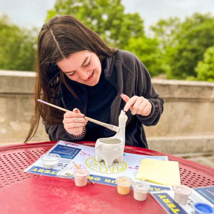 student painting pottery on the MU terrace