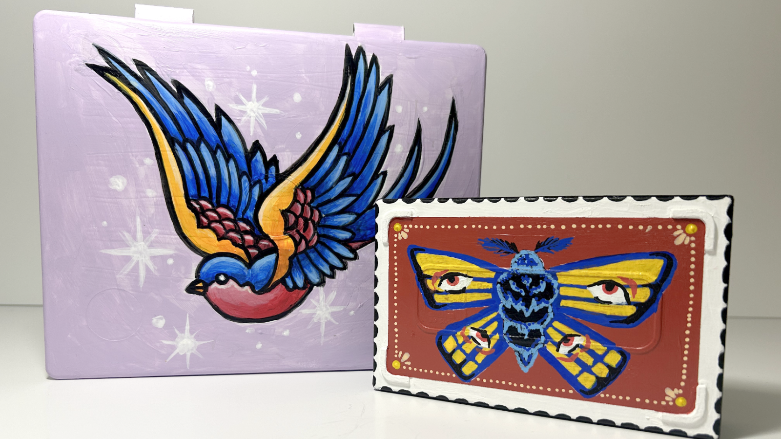 Two trinket box lids. One with a bird and one with a moth painted on them.